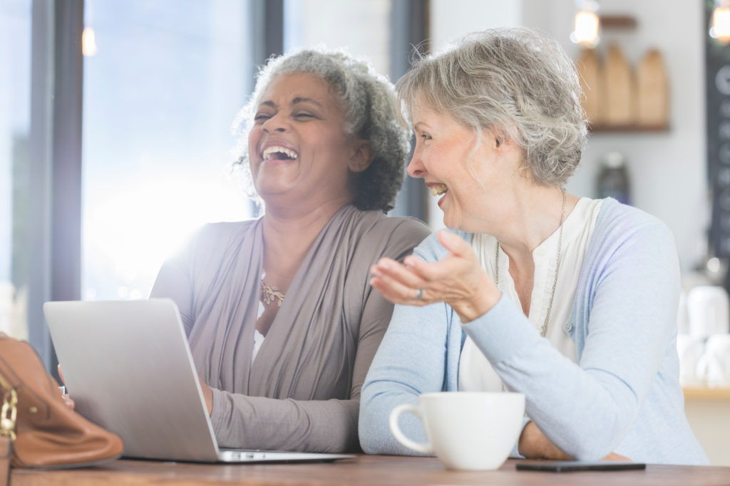 two mature women laughing while enjoying coffee